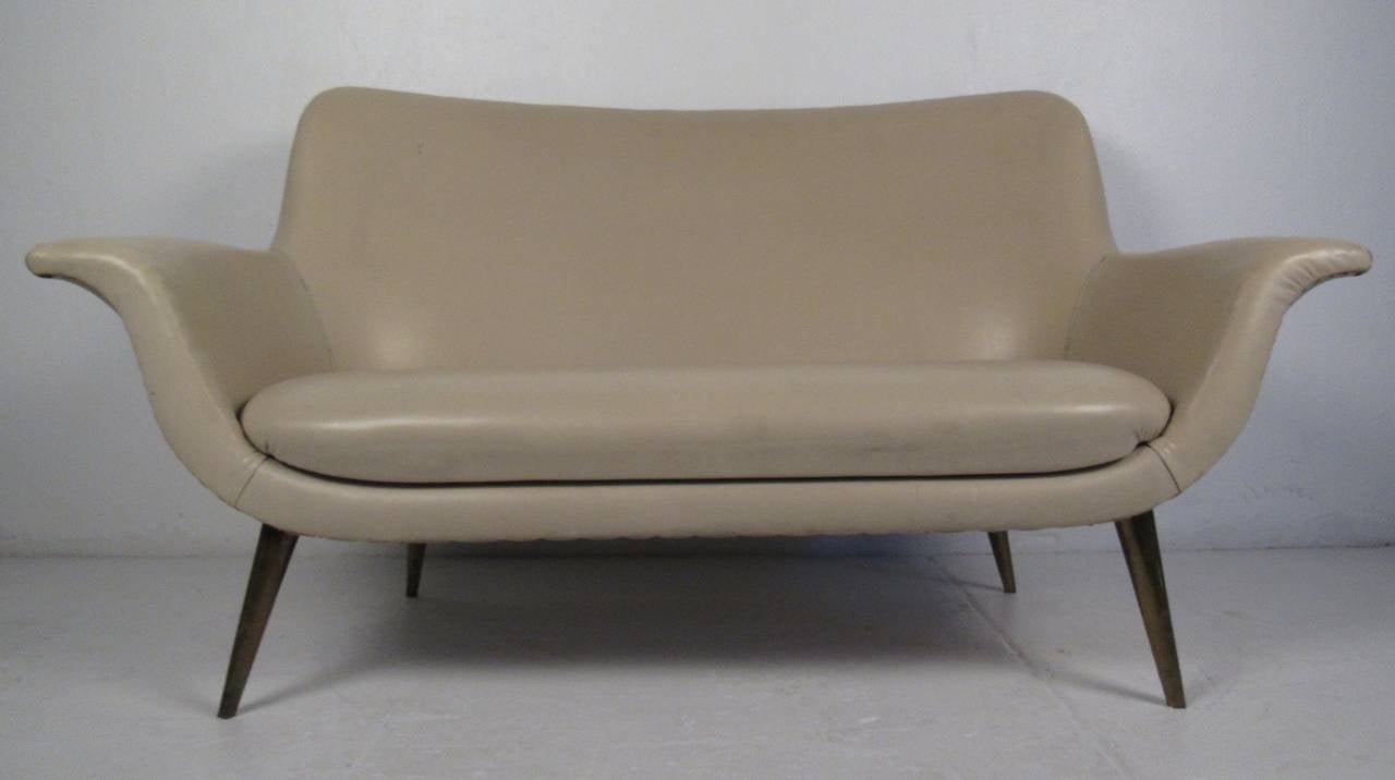 Stylish, sculptural loveseat in warm tan vinyl with brass tack accents and tapered legs.  Impeccable Italian modern design echoes of it's mid-century origins. Impressive sofa for home or office seating. Please confirm item location (NY or NJ) with