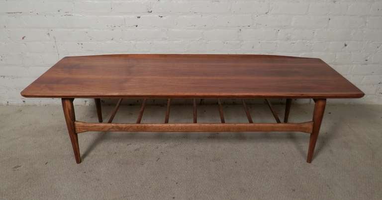 Vintage modern designed walnut coffee table with striking flared edges, tapered legs and a slat shelf for storage. Refinished walnut grain top. A great cocktail table.

(Please confirm item location - NY or NJ - with dealer)