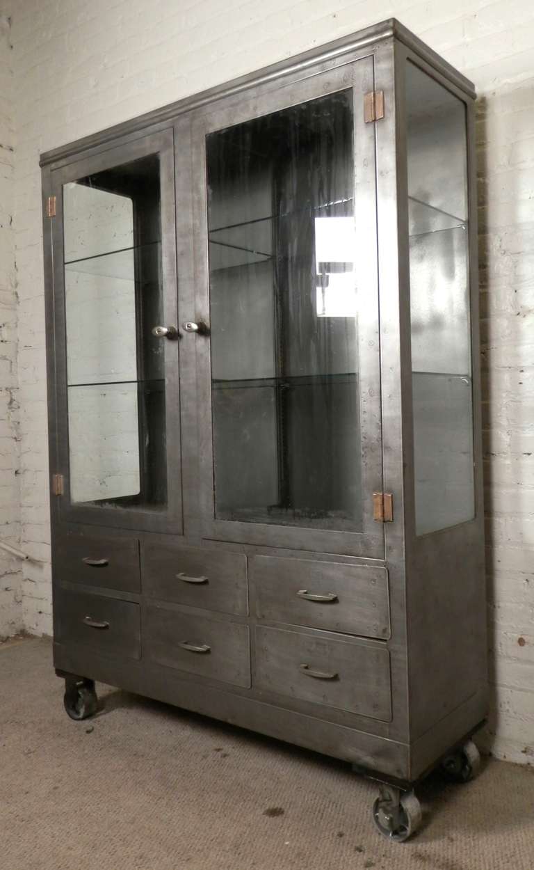 Large industrial metal hospital supply cabinet, newly restored in a rough metal finish, can now fit in nicely to any modern kitchen, living room or store. Glass shelves are adjustable and can easily accommodate many more shelves. Large metal casters