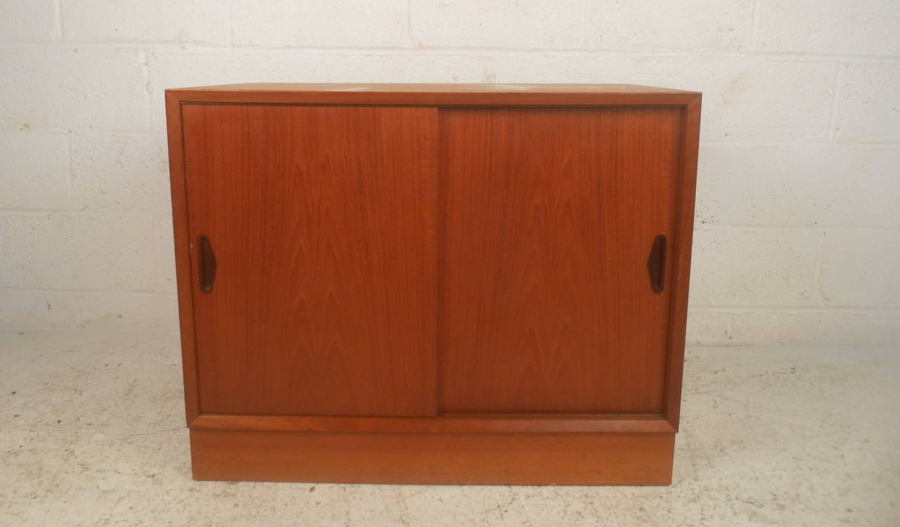 This Danish teak record cabinet features two sliding doors with carved pulls, an adjustable interior shelf, and divider for storing records and forty-fives which offers a modern accent and ample storage to any home or office space.

Please confirm
