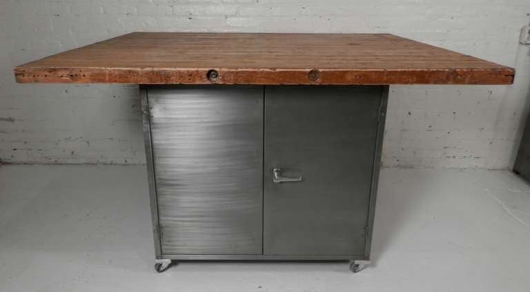 One of a kind rolling table with aged butcher block top fixed to a dual sided metal cabinet. One side features large double doors with locking handle, the reverse side contains four wide drawers complete with original number tags. Put on casters for