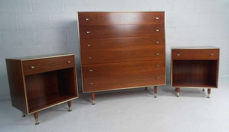 This vintage modern three-piece set includes Mid-Century nightstands and six drawer highboy dresser. This stylish mix of natural wood finish, brass pulls, and tapered legs with brass sabots make this Mid-Century R-Way bedroom set a fantastic