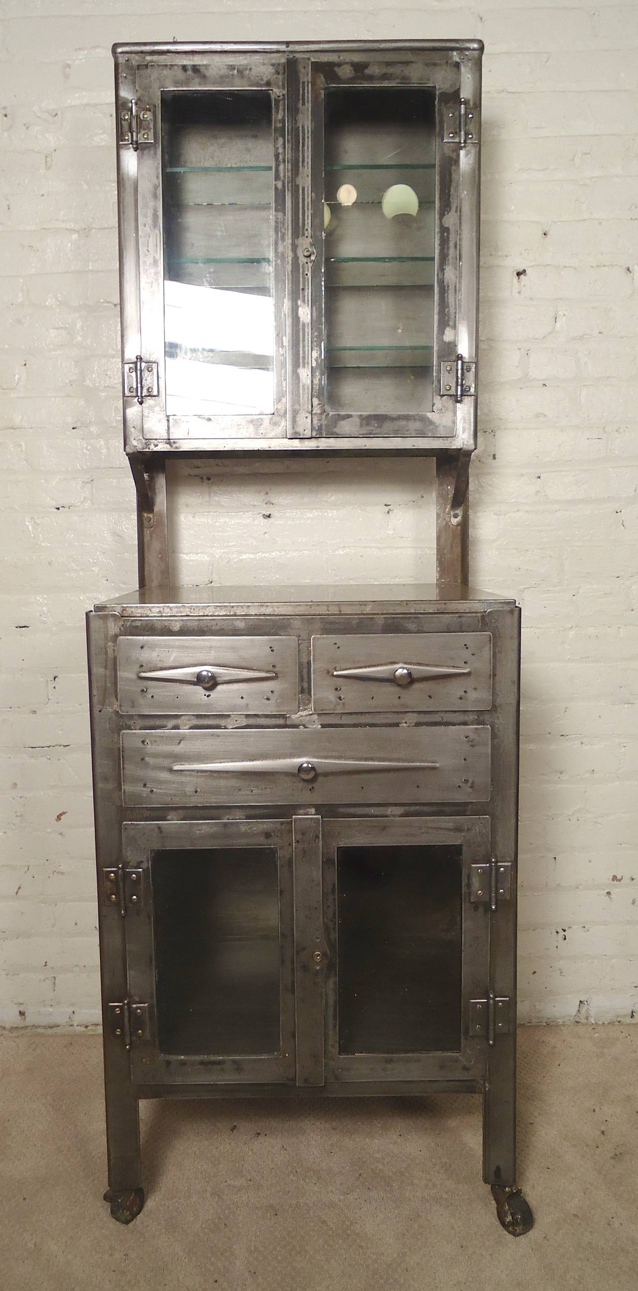 Tall display cabinet with top and bottom transparent storage. Completely restored to a bare metal style finish. Removable glass shelves, drawers and bottom cabinet space, set on rolling casters.

(Please confirm item location - NY or NJ - with