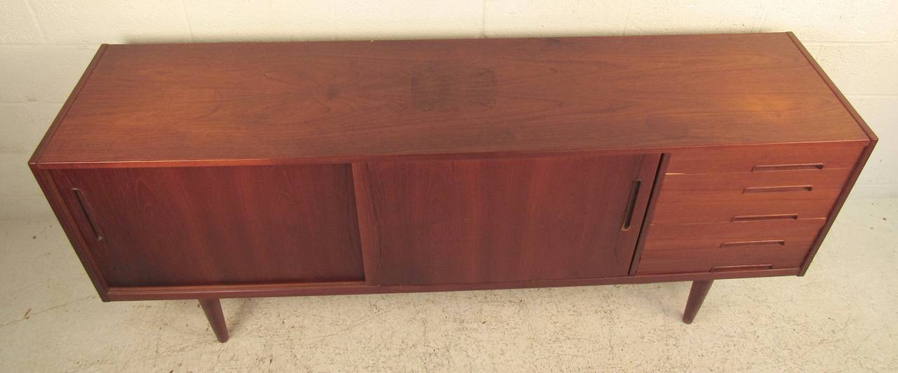 Mid-Century Danish cabinet designed by Nils Jonsson, featuring sliding door cabinet and five-drawers. Vintage Scandinavian teak grain, tapered legs, optional adjustable shelving make this an ideal storage credenza or sideboard for home or office