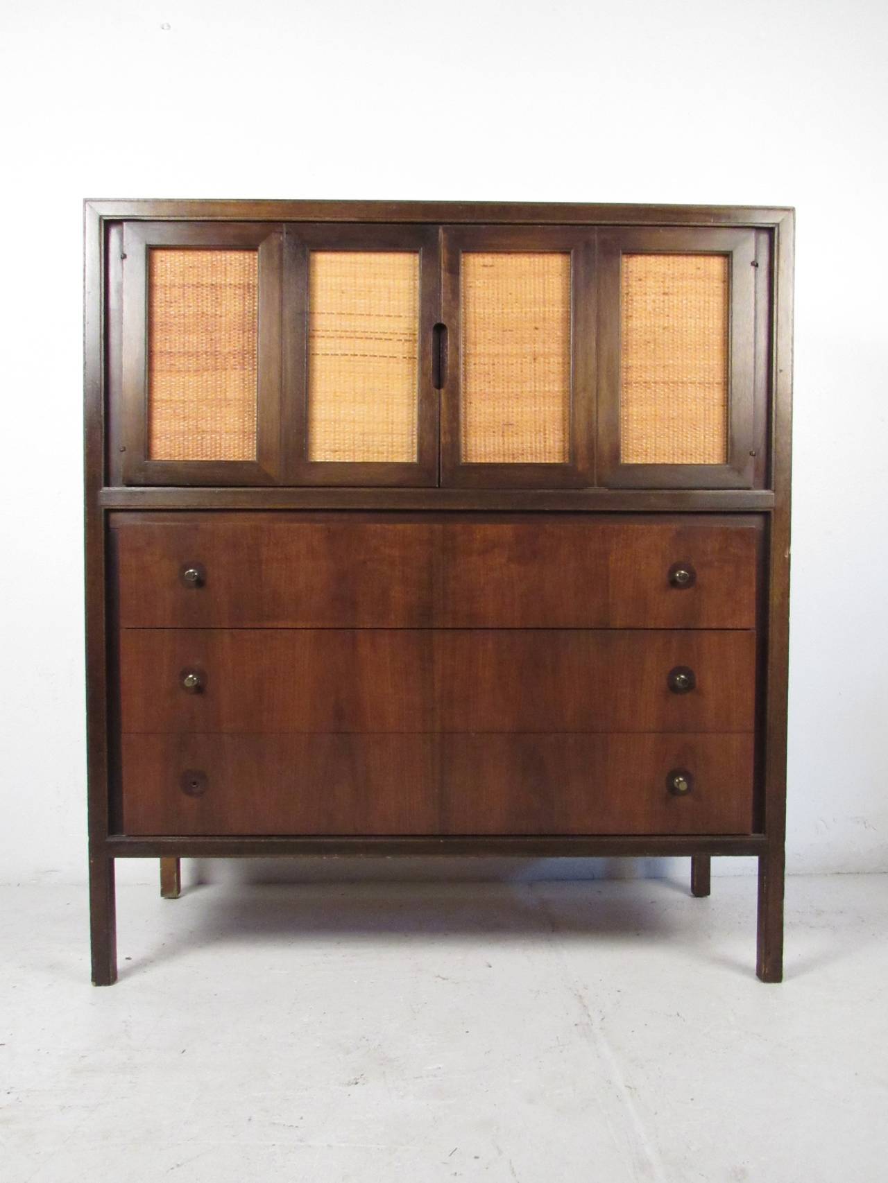 This midcentury high boy dresser by Basic Witz features a beautiful walnut finish, cane doors, and unique brass pulls which offers a modern accent and ample storage to any home or office space. Cane inserts are reversible with a black side