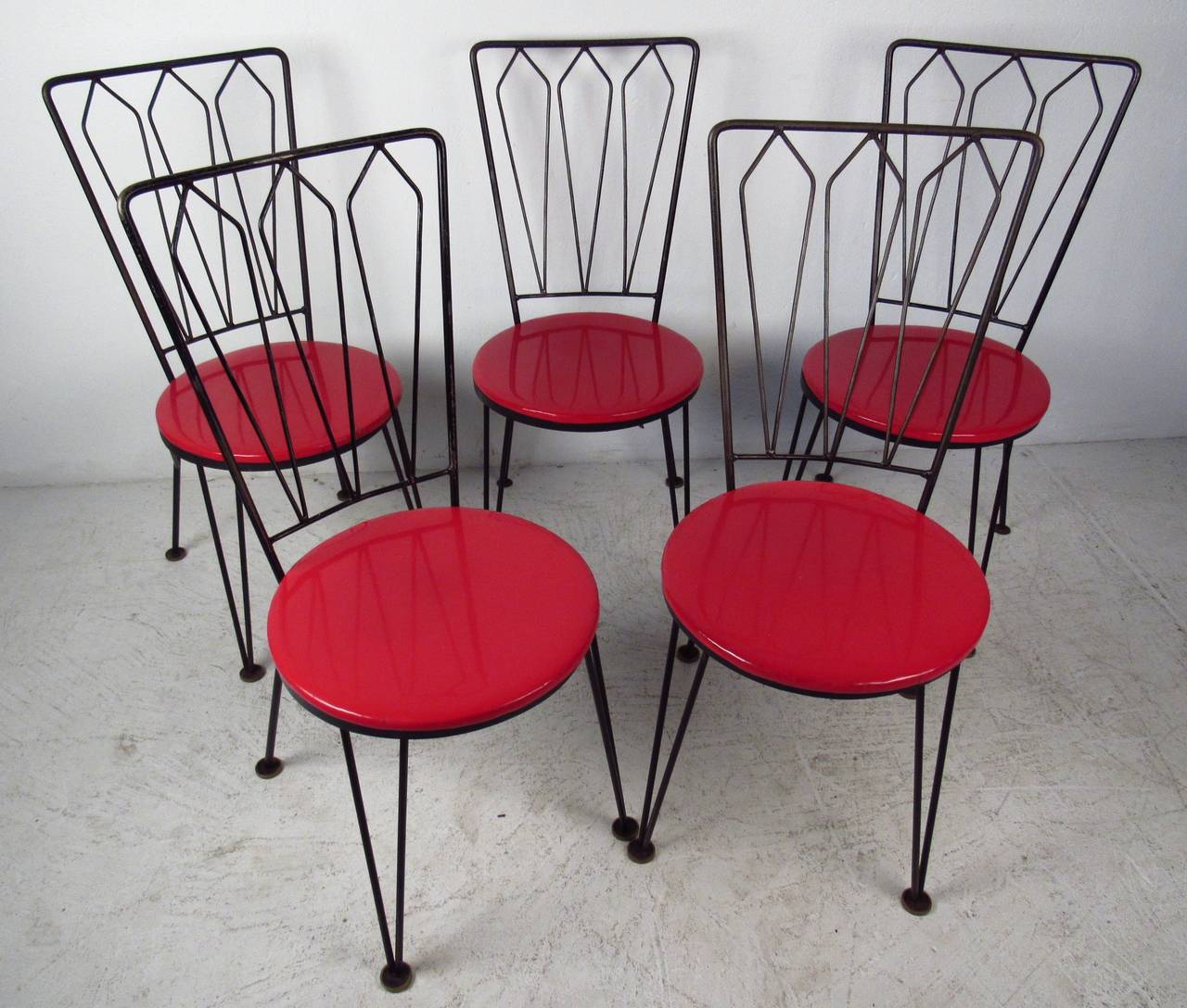 Great set of 1950s retro style metal and vinyl seat dining chairs. A sleek mid-century design with hairpin style legs, geometrical designs on the backrest, and circular cushioned seats covered in cherry red vinyl. Please confirm item location (NY or