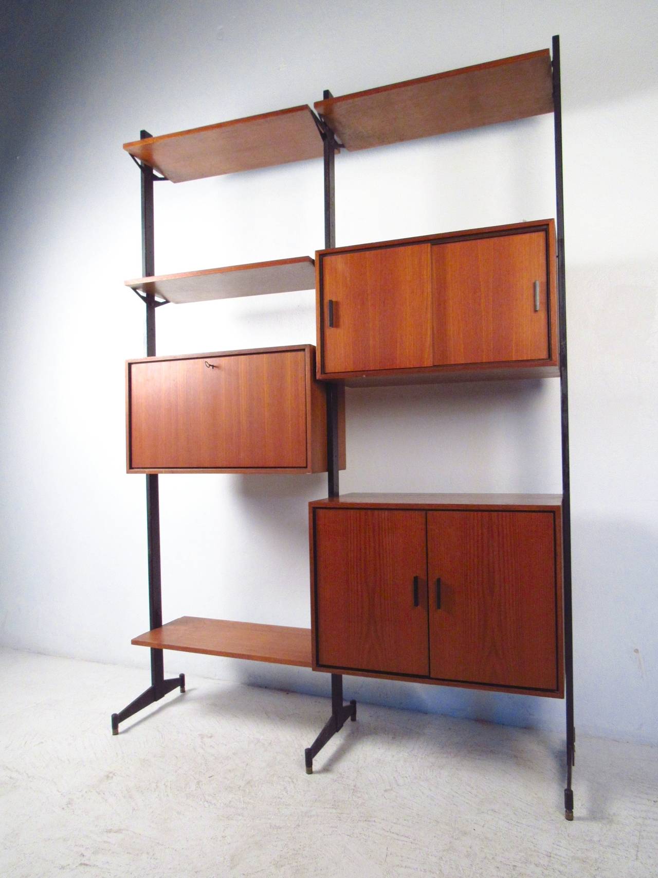 Freestanding modular wall unit with teak shelves and compartments mounted to black metal supports. consists of drop front writing surface, sliding door compartment, and double door storage module. Please confirm item location (NY or NJ) with dealer.