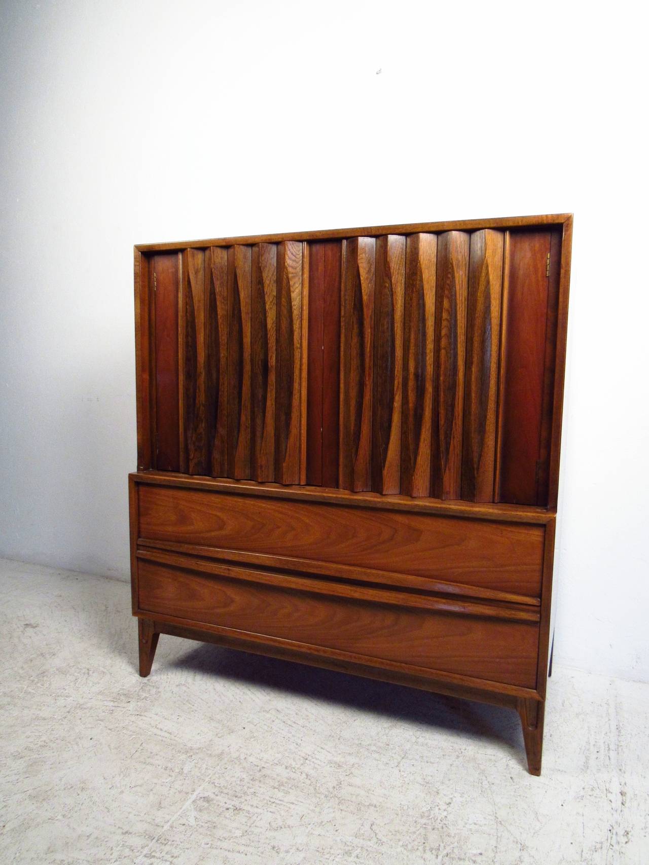 This Mid-Century gentleman's chest features vertical louvered doors, carved drawer pulls and unique tapered legs which offer a modern flare and ample storage to any home or office space. 

Please confirm item location (NY or NJ) with dealer.