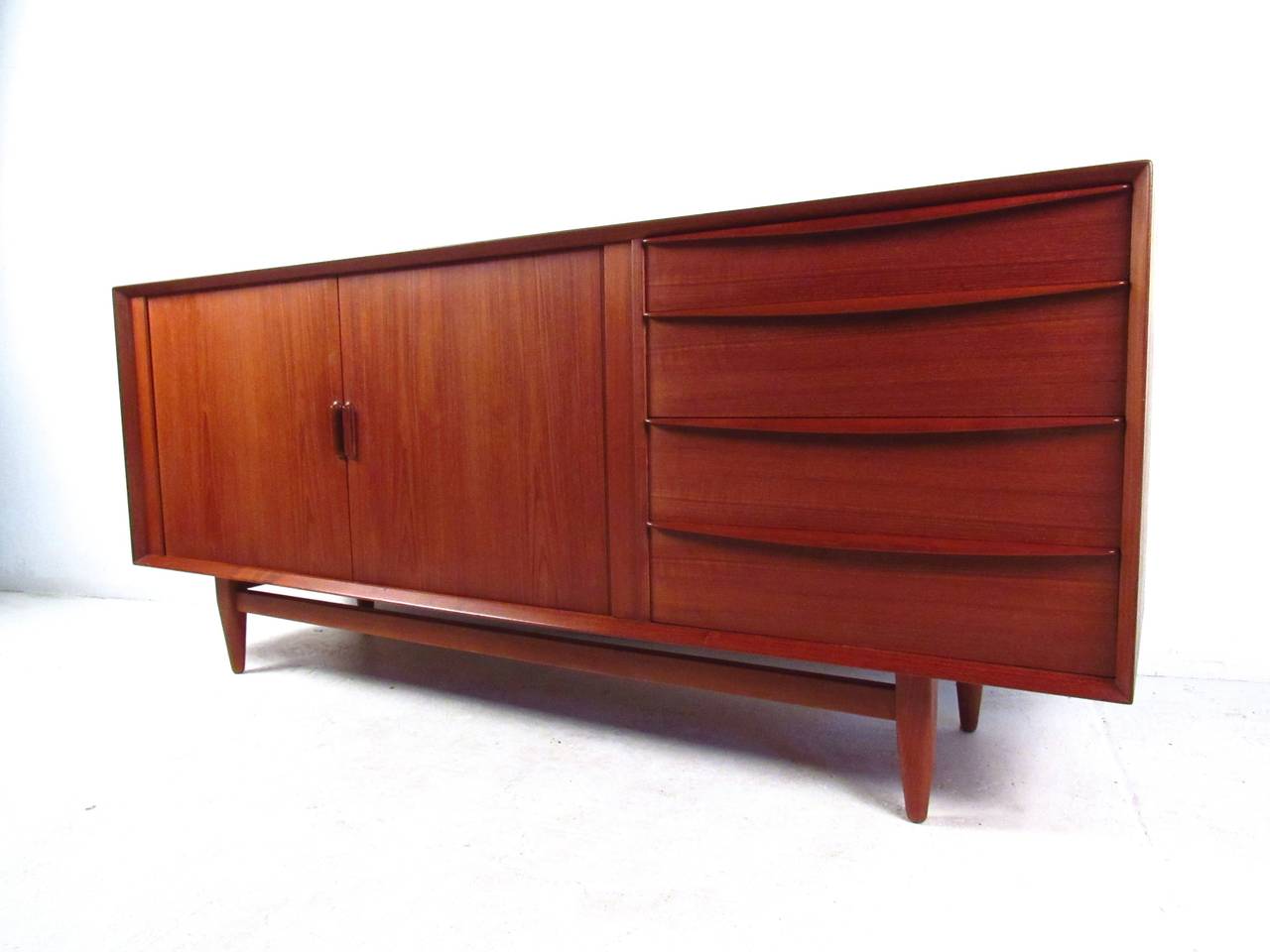 This beautiful midcentury Danish teak sideboard come features plenty of space for storage or display, the beautiful teak veneer, tapered legs, finished back, and unique drawer pulls add to the charm of this Falster tambour sideboard. Please confirm