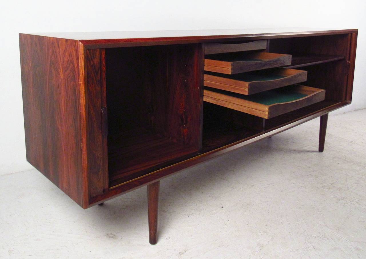 Rich rosewood grain throughout this gorgeous Danish sideboard. Designed by Svend A. Larsen for Faarup Møbelfabrik. Long tambour doors, four sculpted trays, adjustable shelf, tapered legs and brilliant finished back! This is Danish modern design at