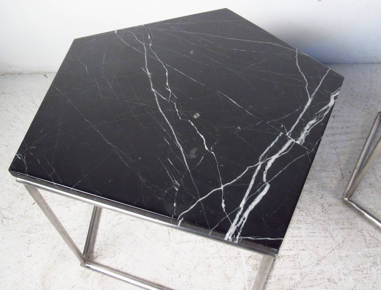 Two vintage-modern side tables, each features a chrome base and a black marble top in the shape of a pentagon. A unique pair that can form a coffee table when placed together. This stylish pair of end tables that's ideal for a living room display or