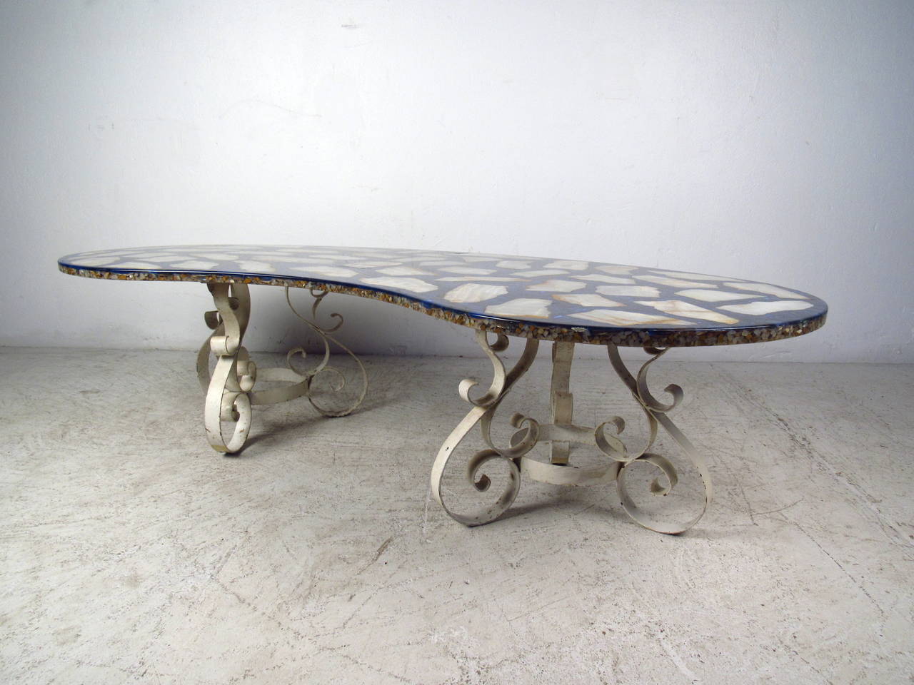Cette table basse italienne du milieu du siècle en forme de rein présente un plateau unique en pierre composite et une base plate en fer forgé. Un design robuste avec des couleurs élaborées sur le dessus et des détails inhabituels de volutes sur la