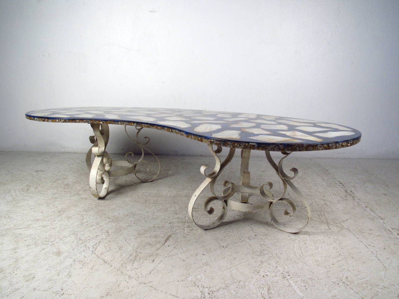 This Italian mid-century kidney shaped coffee table features a unique stone composite top and flat bar iron base. A sturdy design with elaborate colors on the top and unusual scroll detail on the base. This stylish coffee table makes the perfect eye