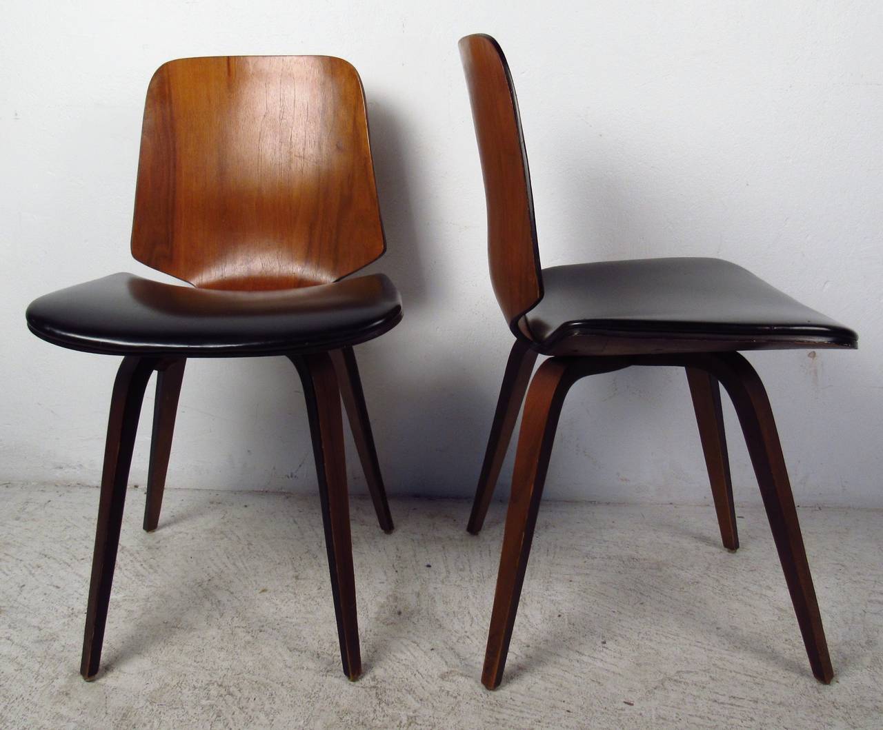 Pair of bentwood and black vinyl chairs by Norman Cherner for Plycraft. A stunning design with a thick padded seat, wide backrest, and tapered legs. This sturdy and stylish pair boasts an elegant walnut wood grain throughout. Please confirm item