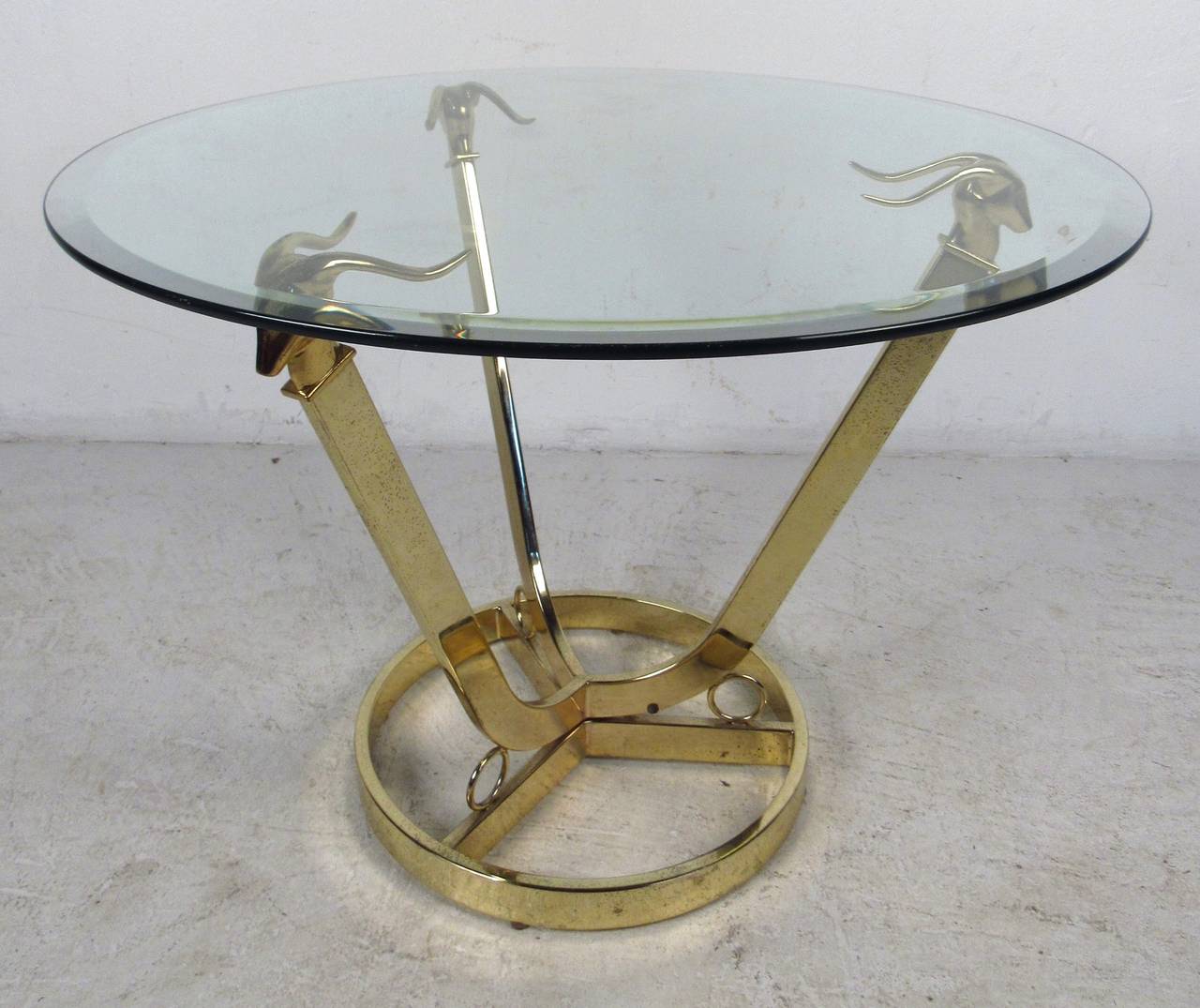 Modern glass top table with flat bar brass-plated three arm base featuring decorative animal head supports. A versatile size that functions as a coffee table or a large side table. This stunning contemporary modern end table makes the perfect eye