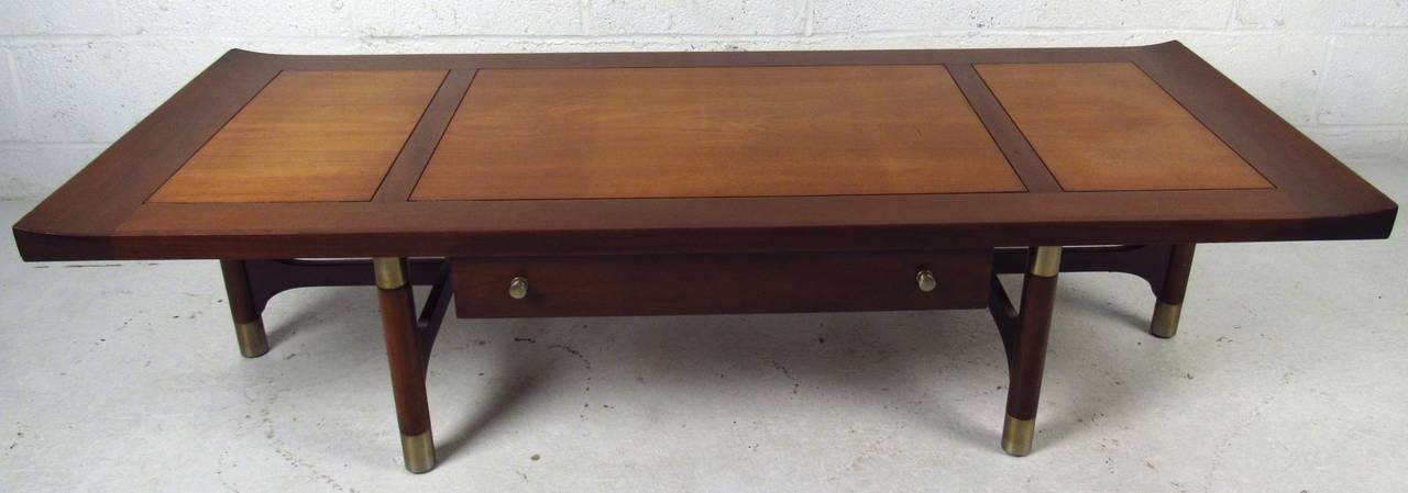 Vintage-modern Weiman coffee table, features beautiful two-tone top, one drawer with silver pulls and sculpted base with unique brass accenting. This Asian style cocktail table is sure to compliment any modern interior.

Please confirm item