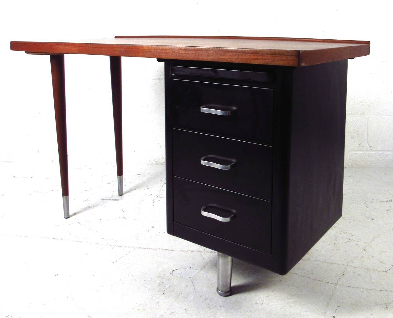 This stylish industrial modern writing desk features right-side three drawer design, Danish teak raised-edge top, and sturdy metal drawer storage. Petite dimensions make this an ideal desk for apartment or home office use. Unique Mid-Century Modern