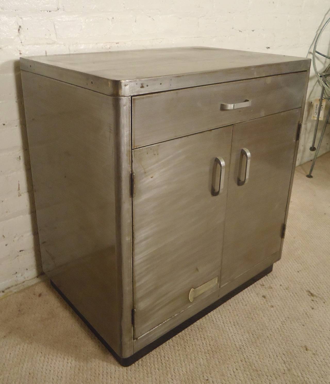 Vintage metal two door cabinet with fantastic bare metal style finish. Drawer and cabinet with shelf storage, original handles and accenting black trim bottom.

(Please confirm item location - NY or NJ - with dealer)