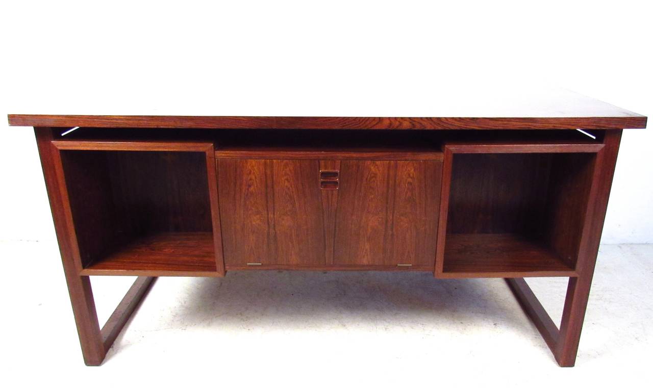 This fantastic vintage desk features unique sled leg design, carved handles, and unique hidden storage on the alternate side. Beautiful rosewood finish and floating top design make this a a stylish addition to any home or office. Please confirm item