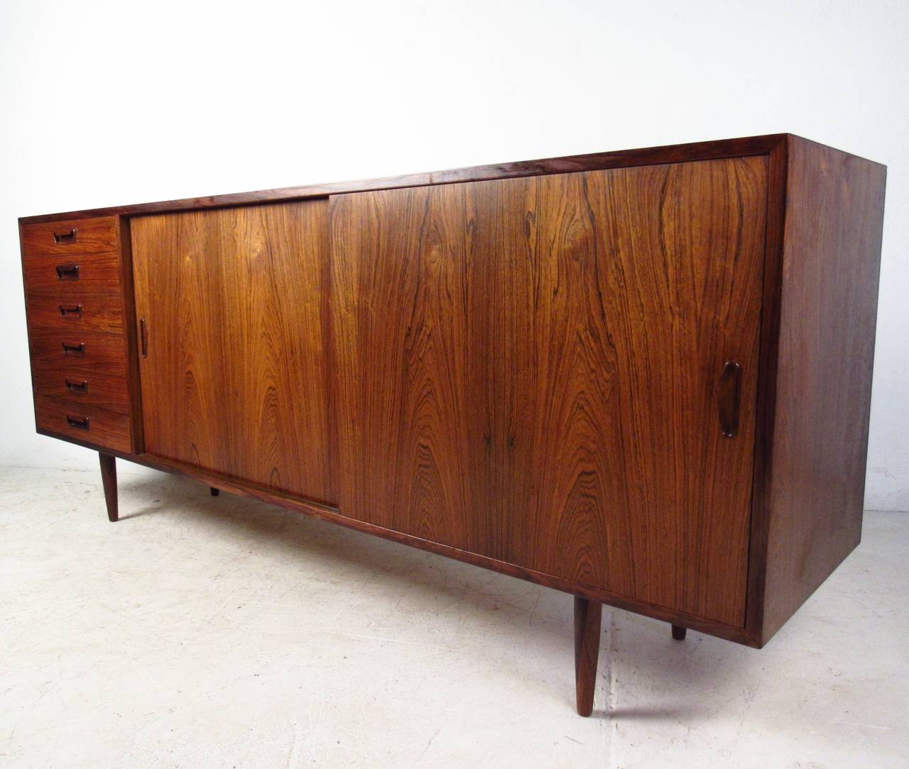 This sliding door sideboard is uniquely sized for smaller serving areas, yet offers plenty of space for storage. Vintage rosewood finish is visually stunning, while carved drawer pulls & tapered legs add to it's appeal. Please confirm item location