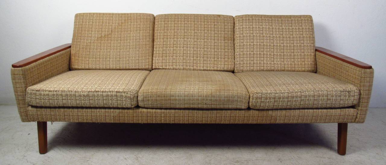 Danish Modern three-seat sofa with teak armrests makes a stylish vintage addition to home or business seating area. Vintage upholstery, stylish mid-century modern design add to the appeal of the piece. Please confirm item location (NY or NJ) with