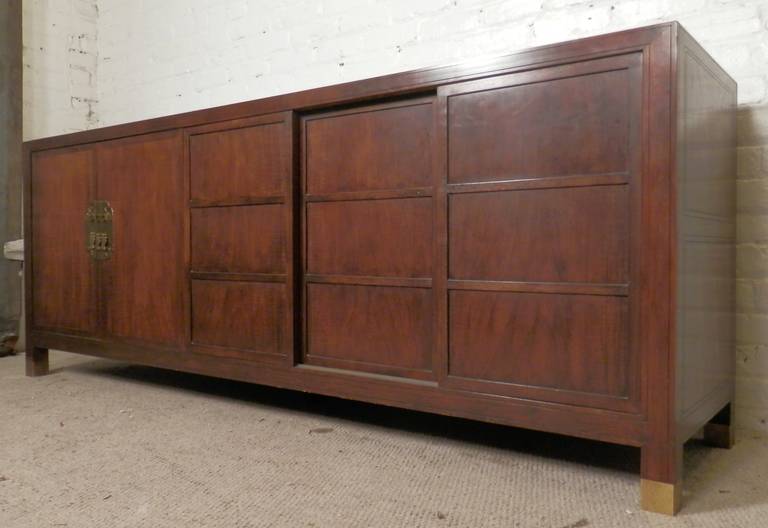 Rare sideboard made by Baker Furniture for their Far East collection. Attractive walnut grain throughout, hinged doors open to drawers and cabinet, large side cabinet with adjustable shelf. Three sliding panel doors moving left and right, great