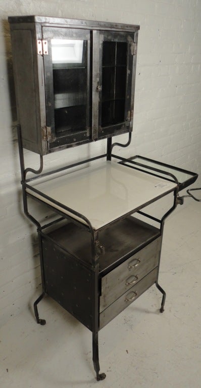 Amazing bare metal dental cabinet with glass doors & shelves, three storage drawers, and white glass work surface.