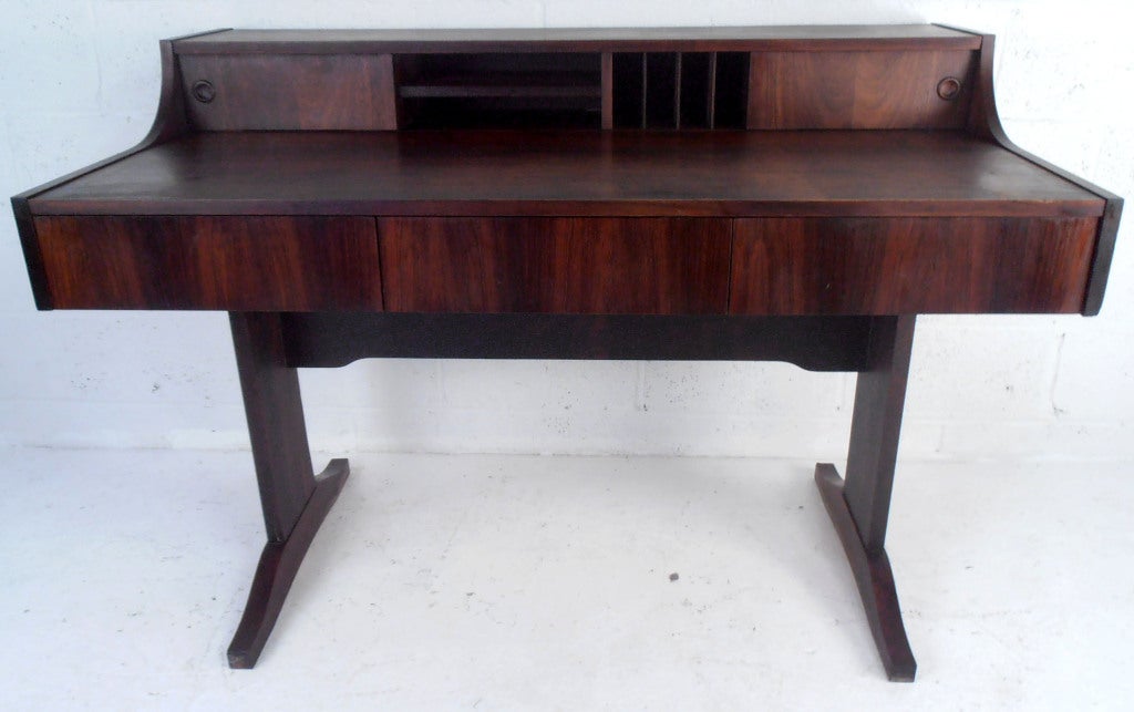This Danish Rosewood desk features a beautiful wide grain veneer and fits in any room. Offering a spacious work area with plenty of room for storage this classic piece is an eye-catching addition to home or office.

(Please confirm item location -
