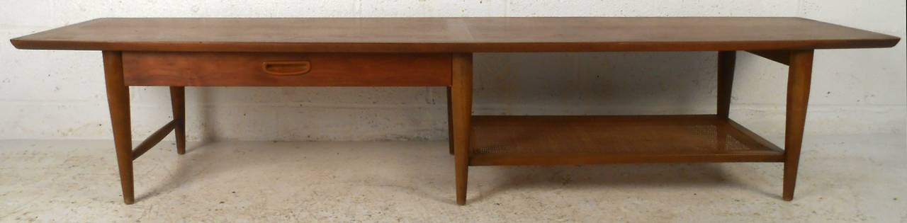 Vintage-modern American made coffee table, features one drawer with carved pull, one cane shelf, sculpted legs and beautiful walnut grain, manufactured by Lane.

Please confirm item location NY or NJ with dealer.