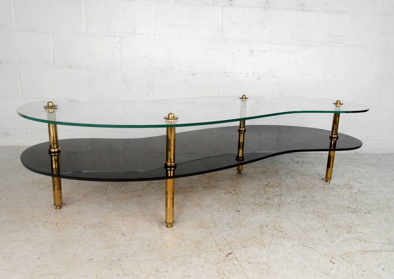 This beautiful coffee table features a stylish mid-century look, combining two tier glass construction with gorgeous brass frame. Thick top glass and flowing free-form shape make this a wonderful centerpiece for home or office. Please confirm item