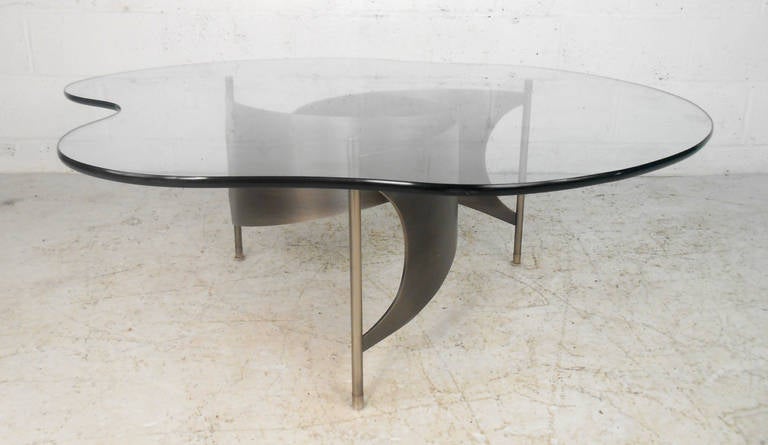 This unique brushed steel coffee table features the beautiful fluid design style of Knut Hesterberg. This well polished fan blade style base features sturdy leg supports, perfect for supporting it's ample free-form glass top. Please confirm item