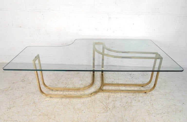 This large and beautifully shaped brass and glass coffee table is a wonderful vintage centerpiece for living or waiting room. While the eye is immediately drawn to the marvelous design of the base, the matching glass top also features a unique