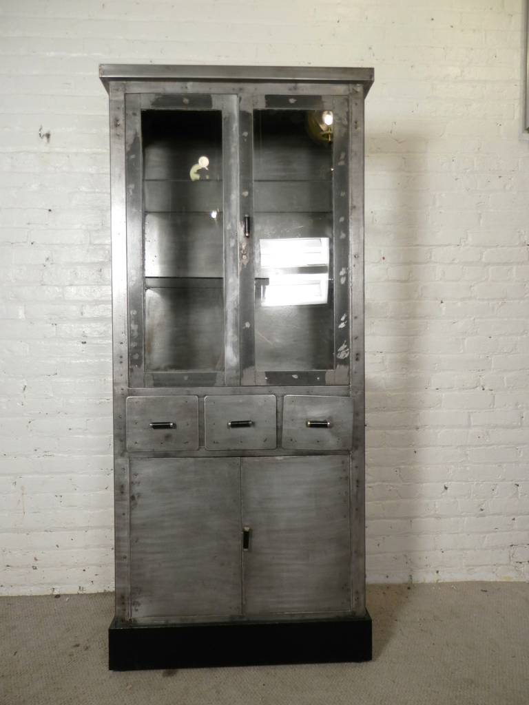 Unusual oversized metal stationary operating room instrument cabinet. Three sided glass cabinet with adjustable glass shelves, three drawers and double door bottom cupboard. 
Heavy duty metal, stripped and restored to a handsome Industrial finish.