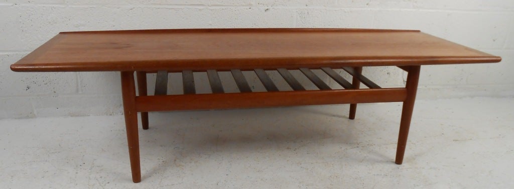 This vintage teak coffee table boasts Scandinavian Modern design, including turned edges and lower slat shelf. Rich teak finish makes a unique Mid-Century addition to any interior. Please confirm item location (NY or NJ).