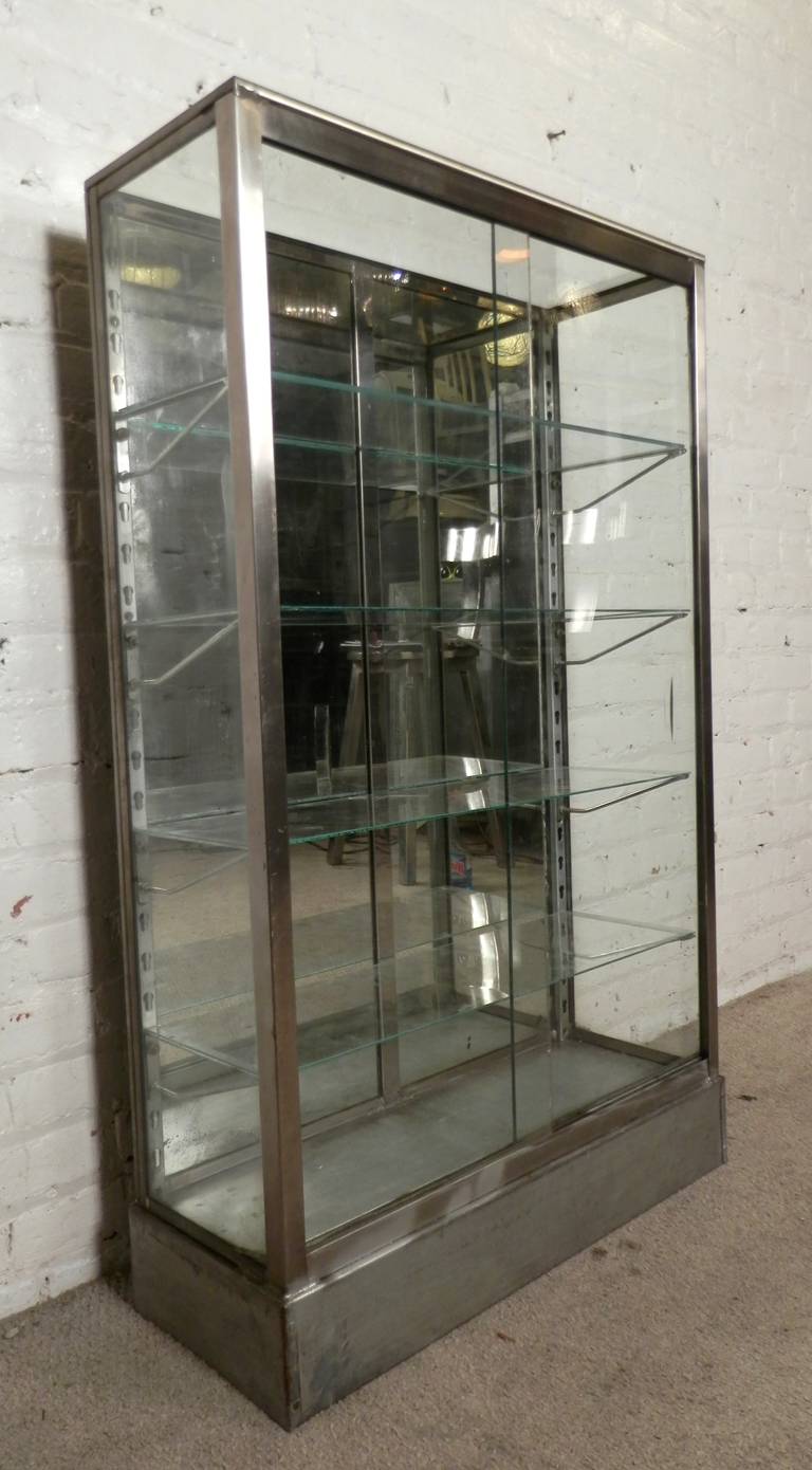 Excellent metal cabinet with three sides of glass, glass top and mirrored back. Sliding glass panel doors open to four adjustable glass shelves. The frame has been restored to a bare metal style finish. A one of a kind display cabinet or