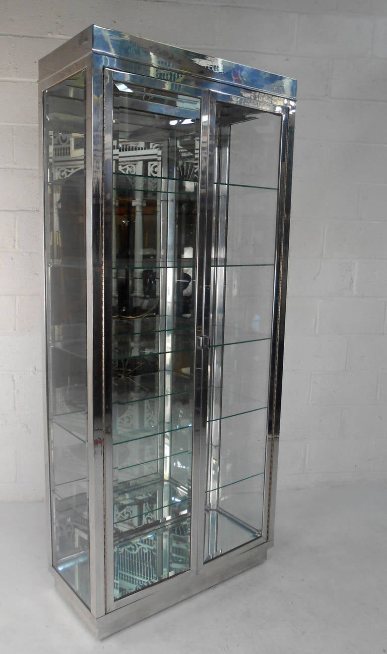 This beautiful vintage display cabinet is a beautiful mix of aluminum with a chrome finish and five spacious glass shelves. The floor and back panel are mirrored, and a light fixture is mounted at the top of the cabinet. Perfect display for home or