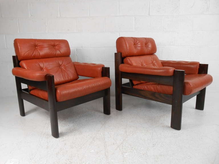 Great pair of comfortable Danish Modern lounge chairs in orange leather, fantastic midcentury Scandinavian design. The elegant wood grain, overstuffed cushions, and padded armrests ensure maximum comfort in any setting. Please confirm item location