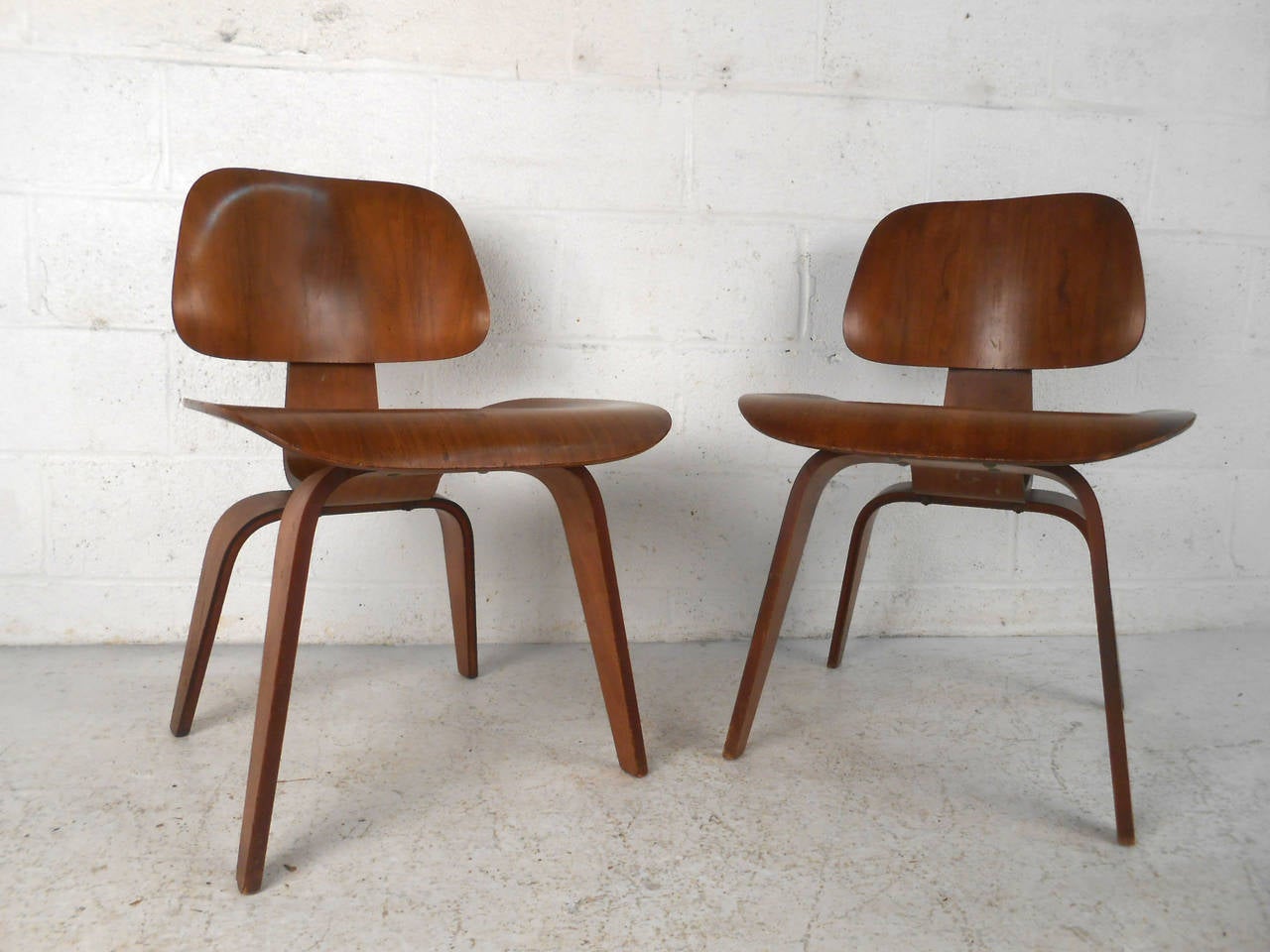 This beautiful matching pair of walnut side chairs designed by Charles and Ray Eames feature the unique molded ply design they were so well known for. Rubber spacers in the back rest and the remnants of an original label featuring the logos of both