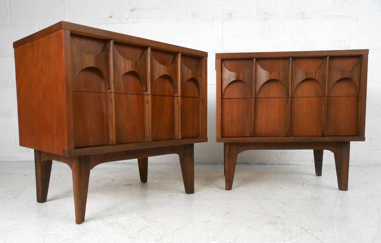 This matching pair of sculpted front walnut end tables feature a unique mid-century look, and two spacious drawers for storage. Dovetailed construction, tapered legs, and fantastic Kent Coffey style design make this pair the perfect addition for any