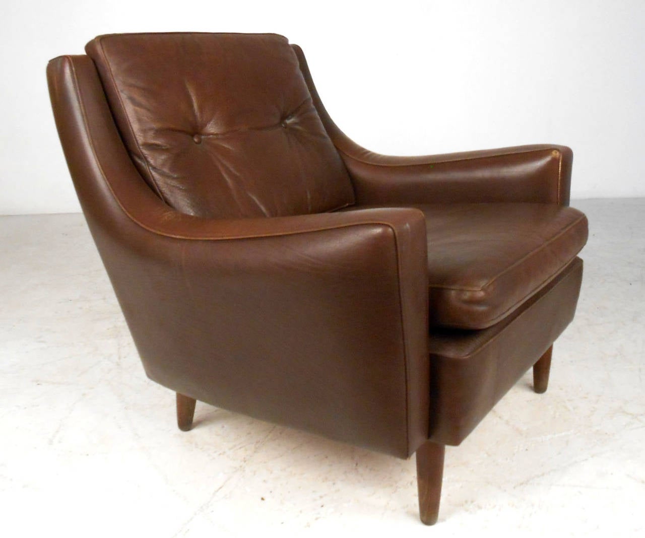 This wonderful low club chair combines classic vintage leather with sturdy walnut frame. Uniquely shaped armrest/seatback design makes this an extremely comfortable seating addition. Uniquely tufted upholstery adds to the chairs mid-century appeal.