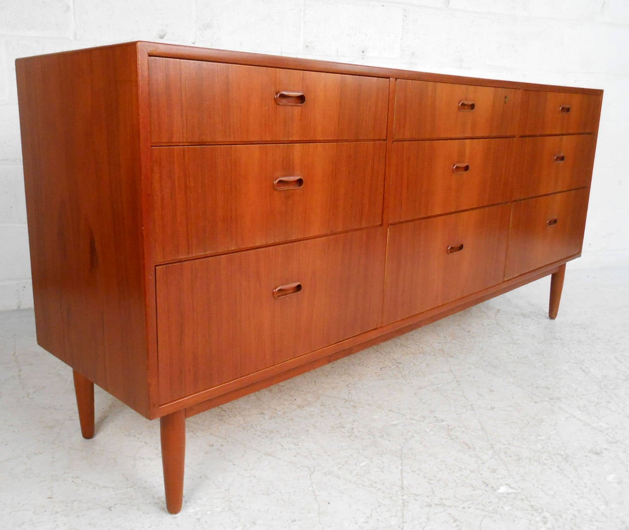 This beautiful Danish teak nine drawer dresser features unique drawer pulls, well-crafted dovetailed drawers, tapered legs, and an exquisite mid-century teak finish. Please confirm item location (NY or NJ).