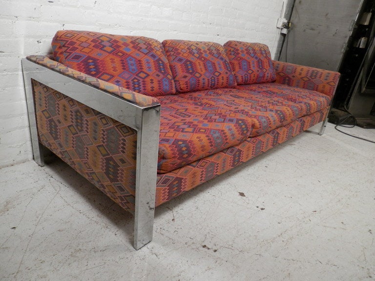 Mid-Century Modern chrome frame sofa in a Milo Baughman style. Awesome vintage pattern with vibrant colors. Sleek polished chrome trim along the arms and down to the floor. The pattern of the upholstery is very attractive and the chrome is still