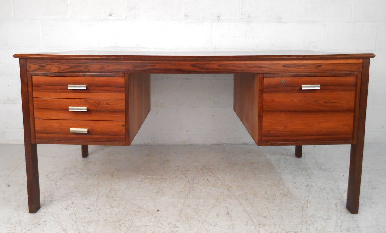This fantastic mid-century desk features a beautiful Rosewood finish, sturdy frame, nad finished back. Unique drawer pulls add to the modern style of the piece, while the ample drawer space is perfect for organization. Please confirm item location