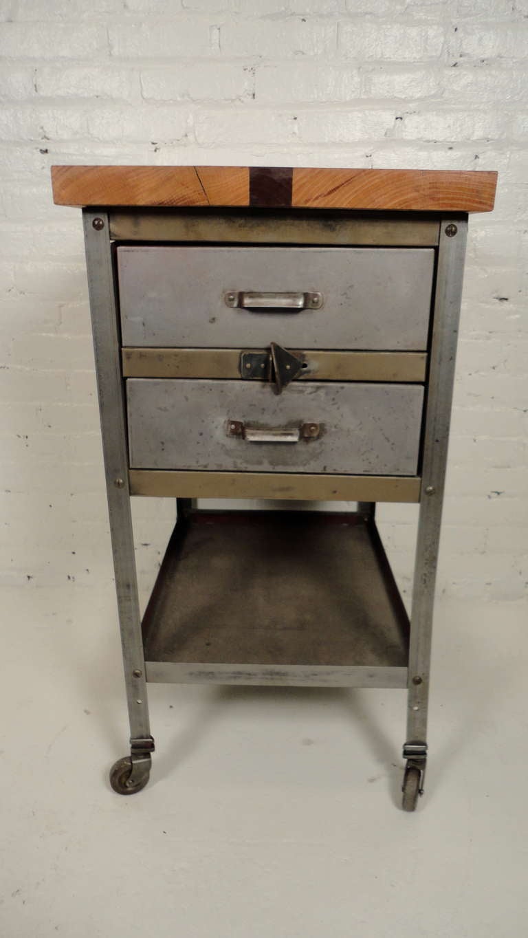 Cabinet made of industrial metal with a dual-tone wood top of oak and rosewood. This piece has two drawers, a shelf, and castors for mobility. Sides adorned with original red paint. Perfect for kitchen or workspace.

(Please confirm item location