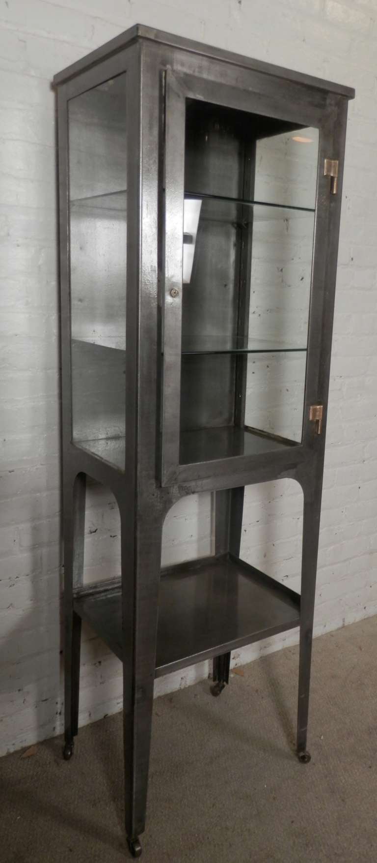 Metal cabinet with three glass sides, two glass shelves, nice brass accenting hardware. Attractive bare metal finish cabinet on casters, perfect for storage or display.

(Please confirm item location - NY or NJ - with dealer)