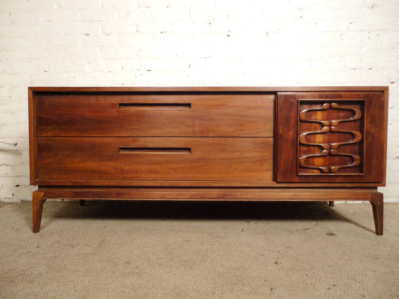 Mid-Century Modern low dresser with sculpted sliding door. Full walnut grain throughout, wide dresser drawers and two smaller drawers hidden by the Witco style gliding door. Makes a great console, credenza or dresser.

(Please confirm item