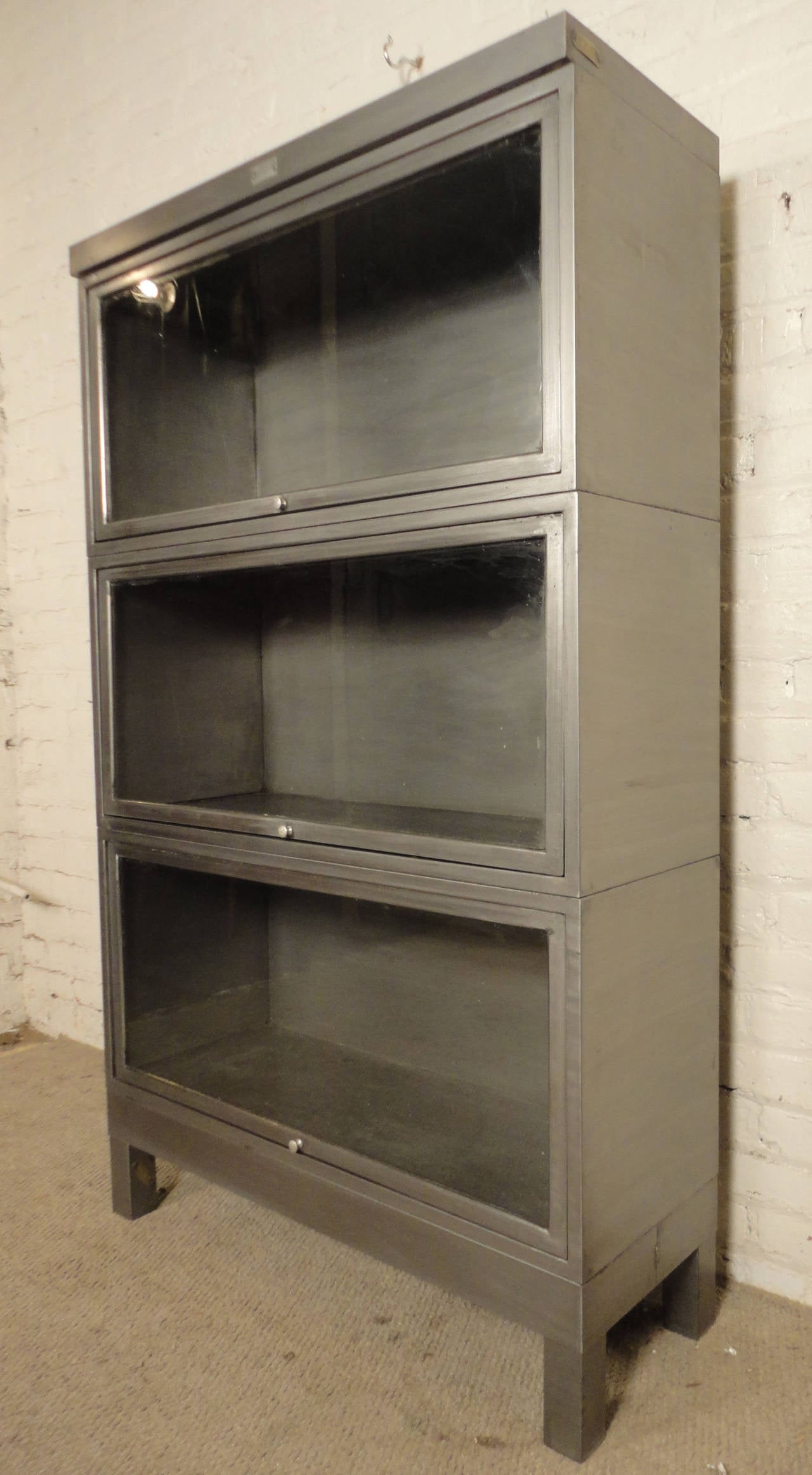 Industrial metal barrister bookcase, stacks three high. Glass window on each unit with polished brass handle. Vintage lawyer bookcase, refinished with a bare metal style for the modern home or office.
Individual Barrister Height - 18

(Please