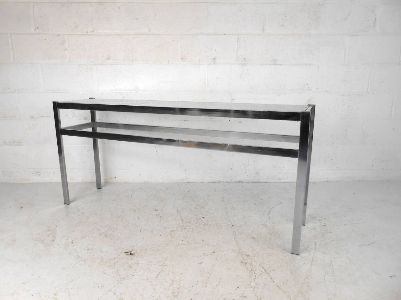 This polished chrome console table features a beveled glass top accented with brass detailing which offers a contemporary flare to any home or office space.  Please confirm item location (NY or NJ) with dealer.