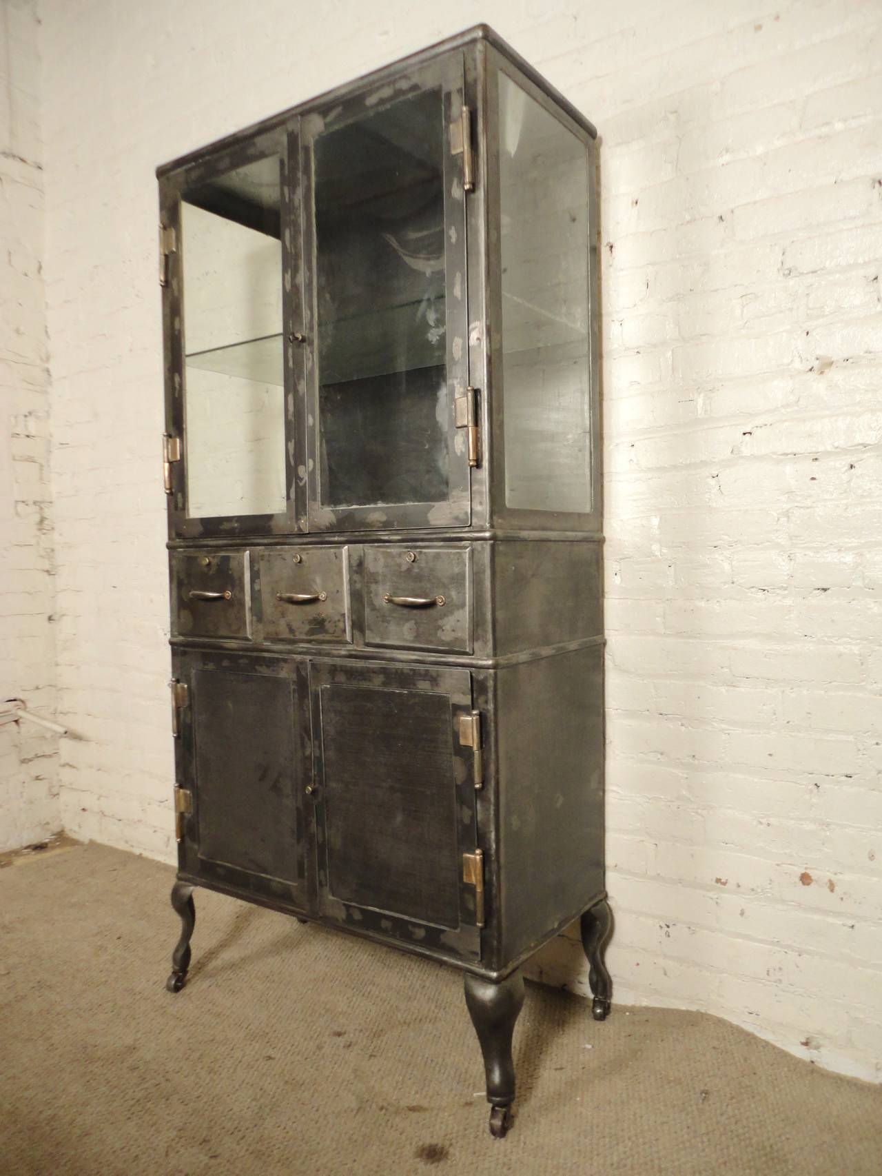 Tall hospital operating room cabinet refinished in a handsome bare metal style finish. Three glass side display top with glass shelf, three drawer and wide cabinet base. Set upon rolling casters for easy mobility, vintage lock units on all drawers