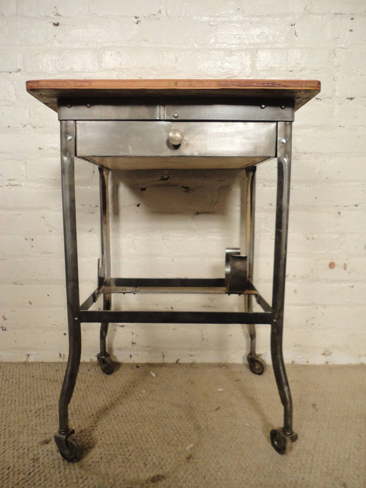 Freestanding American rolling examination room workstation with single sliding drawer, wood top and rolling casters. Used for medical purposes in the early to mid 20th Century, now refinished with a striking bare metal finish for modern use in home